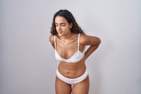 Photo for Young hispanic woman wearing white lingerie suffering of backache, touching back with hand, muscular pain - Royalty Free Image