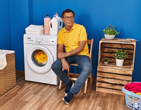 Téléchargez les photos : Middle age man sitting on chair waiting for washing machine at laundry room - en image libre de droit