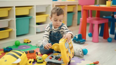 Foto de Adorable caucasian boy playing with toys sitting on floor at kindergarten - Imagen libre de derechos