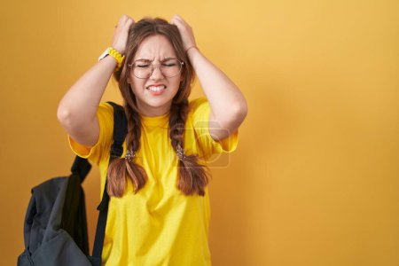 Téléchargez les photos : Jeune femme caucasienne portant un sac à dos étudiant sur fond jaune souffrant de maux de tête désespérés et stressés parce que la douleur et la migraine. mains sur la tête. - en image libre de droit