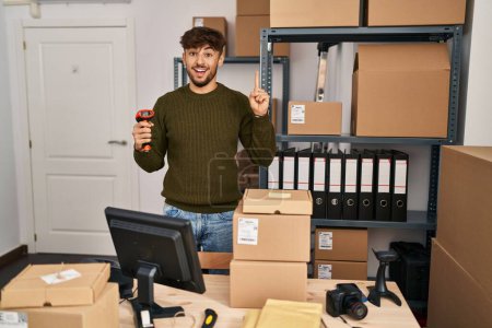 Foto de Arab man with beard working at small business commerce holding bar code scanner smiling with an idea or question pointing finger with happy face, number one - Imagen libre de derechos