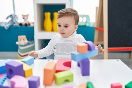 Foto de Adorable bebé caucásico jugando con bloques de construcción de pie en el jardín de infantes - Imagen libre de derechos