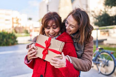 Photo for Two women mother and daughter hugging each other surprise with gift at park - Royalty Free Image