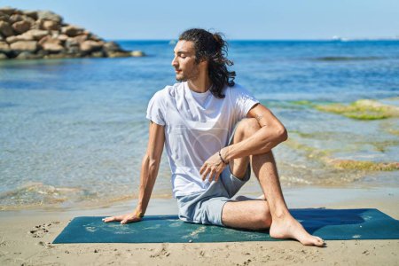 Téléchargez les photos : Young hispanic man doing yoga exercise sitting on sand at beach - en image libre de droit