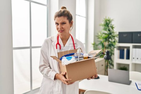 Foto de Young doctor woman holding box with medical items clueless and confused expression. doubt concept. - Imagen libre de derechos