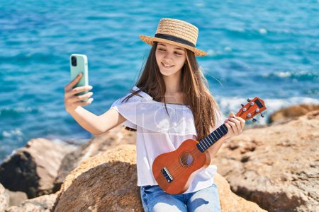 Téléchargez les photos : Adorable girl tourist make selfie by the smartphone playing ukulele at seaside - en image libre de droit