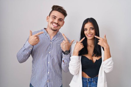 Téléchargez les photos : Young hispanic couple standing over white background smiling cheerful showing and pointing with fingers teeth and mouth. dental health concept. - en image libre de droit