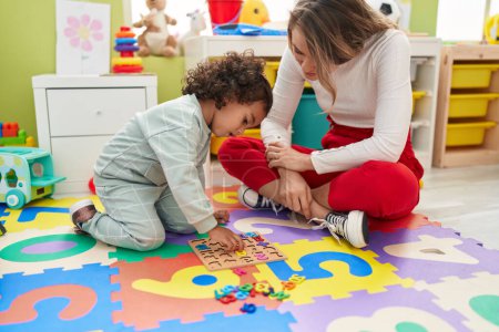 Téléchargez les photos : Professeur et tout-petit jouant avec le jeu de puzzle des mathématiques assis sur le sol à la maternelle - en image libre de droit