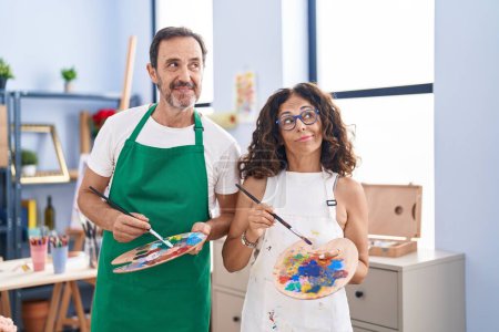 Foto de Middle age hispanic couple painting at art studio smiling looking to the side and staring away thinking. - Imagen libre de derechos