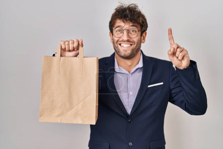 Photo for Hispanic business man holding delivery bag surprised with an idea or question pointing finger with happy face, number one - Royalty Free Image