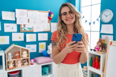 Photo for Young blonde woman teacher using smartphone standing at kindergarten - Royalty Free Image