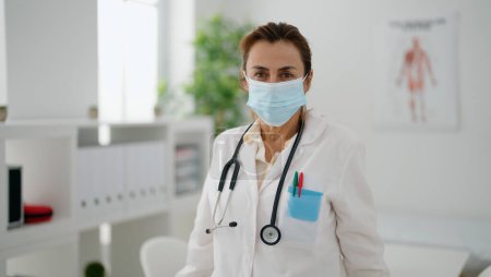 Photo for Middle age hispanic woman wearing doctor uniform and medical mask at clinic - Royalty Free Image