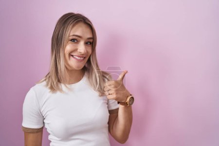 Photo for Blonde caucasian woman standing over pink background doing happy thumbs up gesture with hand. approving expression looking at the camera showing success. - Royalty Free Image