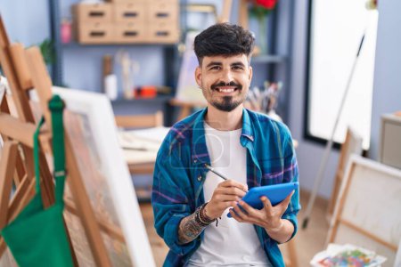 Téléchargez les photos : Young hispanic man artist smiling confident drawing on touchpad at art studio - en image libre de droit