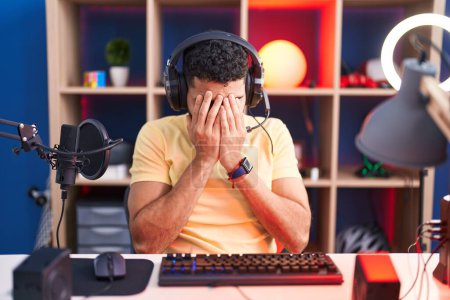 Téléchargez les photos : Hispanic man with beard playing video games with headphones with sad expression covering face with hands while crying. depression concept. - en image libre de droit