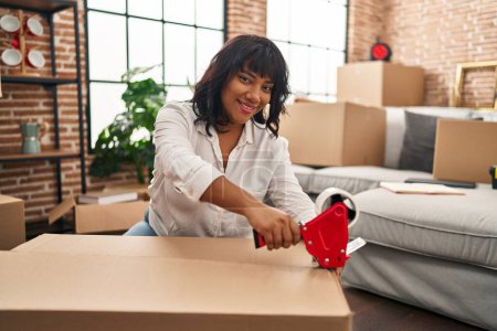 Photo for Young beautiful latin woman smiling confident packing cardboard box at new home - Royalty Free Image