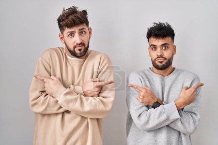 Téléchargez les photos : Young homosexual couple standing over white background pointing to both sides with fingers, different direction disagree - en image libre de droit