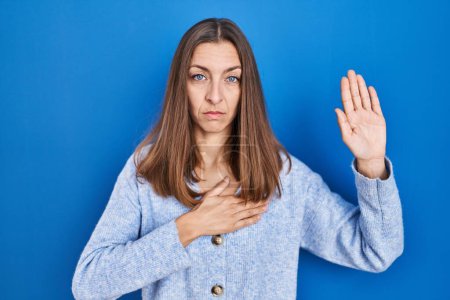 Photo for Young woman standing over blue background swearing with hand on chest and open palm, making a loyalty promise oath - Royalty Free Image