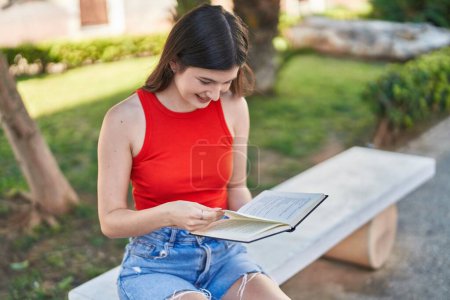Téléchargez les photos : Jeune femme caucasienne lecture livre assis sur banc au parc - en image libre de droit