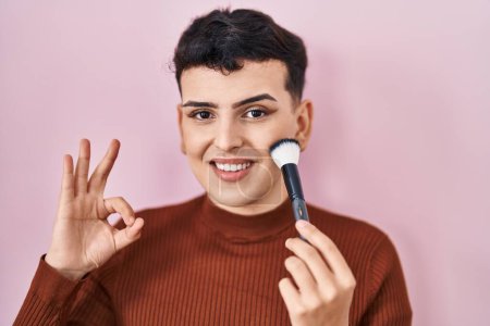 Photo for Non binary person applying make up doing ok sign with fingers, smiling friendly gesturing excellent symbol - Royalty Free Image