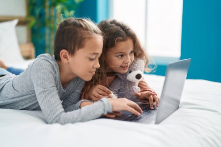 Téléchargez les photos : Deux enfants regardant un film sur ordinateur portable couché sur le lit dans la chambre - en image libre de droit