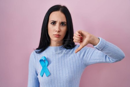 Téléchargez les photos : Hispanic woman wearing blue ribbon with angry face, negative sign showing dislike with thumbs down, rejection concept - en image libre de droit