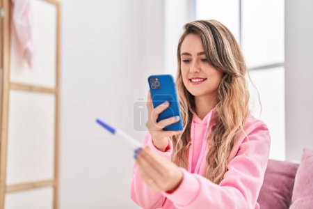 Téléchargez les photos : Young woman make photo by smartphone to pregnancy test at bedroom - en image libre de droit