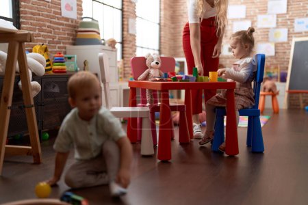 Téléchargez les photos : Professeur avec garçon et fille jouant avec des jouets assis sur la table à la maternelle - en image libre de droit