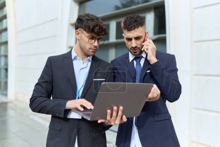 Téléchargez les photos : Two hispanic men business workers using laptop talking on smartphone at street - en image libre de droit