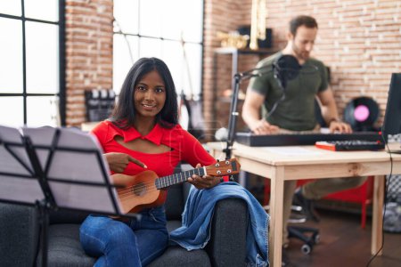 Photo for Young indian woman playing ukulele at music studio smiling happy pointing with hand and finger - Royalty Free Image