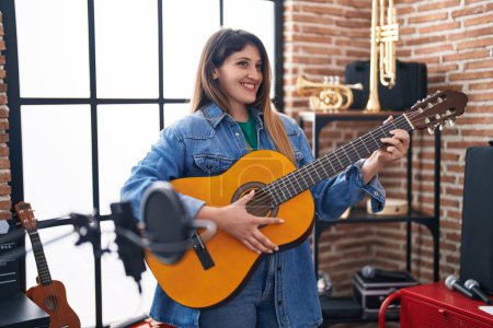 Photo for Young hispanic woman musician playing classical guitar at music studio - Royalty Free Image