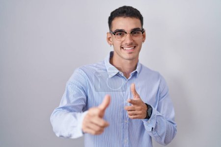 Téléchargez les photos : Un bel homme hispanique portant des vêtements de travail et des lunettes pointant du doigt la caméra avec un visage heureux et drôle. bonne énergie et vibes. - en image libre de droit
