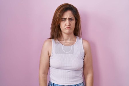 Photo for Brunette woman standing over pink background skeptic and nervous, frowning upset because of problem. negative person. - Royalty Free Image