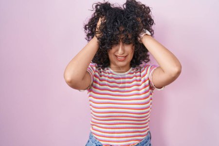 Foto de Young middle east woman standing over pink background suffering from headache desperate and stressed because pain and migraine. hands on head. - Imagen libre de derechos