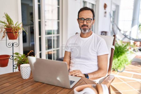 Photo for Middle age man using computer laptop at home puffing cheeks with funny face. mouth inflated with air, crazy expression. - Royalty Free Image