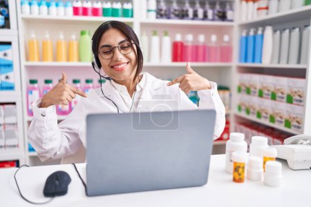 Foto de Mujer árabe joven que trabaja en la farmacia usando un ordenador portátil que se ve confiado con sonrisa en la cara, señalándose con los dedos orgullosos y felices. - Imagen libre de derechos