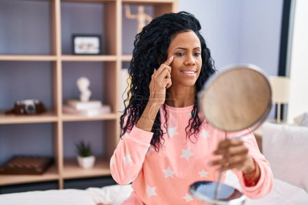 Téléchargez les photos : African american woman looking face on mirror sitting on face at bedroom - en image libre de droit