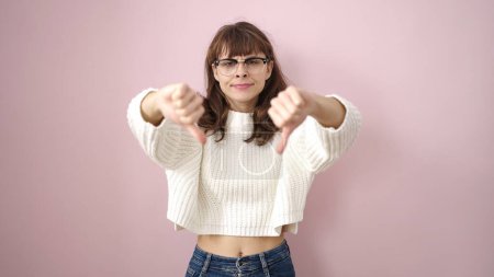 Foto de Young caucasian woman doing negative sign with thumbs down over isolated pink background - Imagen libre de derechos
