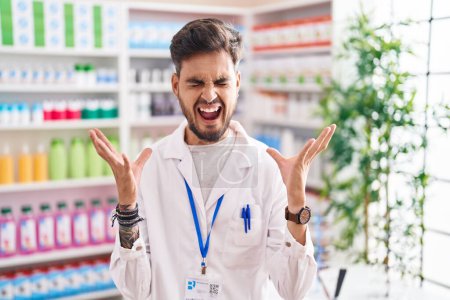 Téléchargez les photos : Jeune homme hispanique avec des tatouages travaillant à la pharmacie pharmacie célébrant fou et fou de succès avec les bras levés et les yeux fermés hurlant excité. concept gagnant - en image libre de droit
