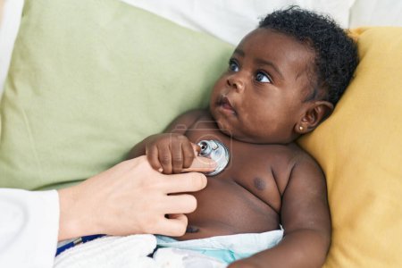 Téléchargez les photos : Bébé afro-américain ayant un examen médical assis sur le lit dans la chambre - en image libre de droit