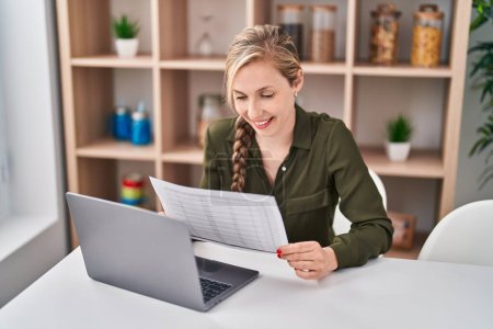 Téléchargez les photos : Jeune femme blonde utilisant un document de lecture d'ordinateur portable à la maison - en image libre de droit