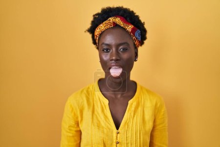 Foto de African young woman wearing african turban sticking tongue out happy with funny expression. emotion concept. - Imagen libre de derechos