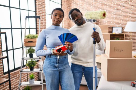 Photo for Young african american couple moving to a new home choosing walls color relaxed with serious expression on face. simple and natural looking at the camera. - Royalty Free Image