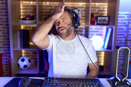 Téléchargez les photos : Middle age man with beard playing video games wearing headphones surprised with hand on head for mistake, remember error. forgot, bad memory concept. - en image libre de droit