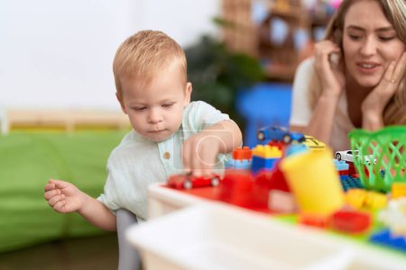 Photo for Teacher and toddler playing with construction blocks and car toy sitting on table at kindergarten - Royalty Free Image