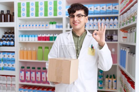 Foto de Joven hombre no binario que trabaja en farmacia caja de espera de farmacia haciendo signo bien con los dedos, sonriendo gesto amistoso excelente símbolo - Imagen libre de derechos