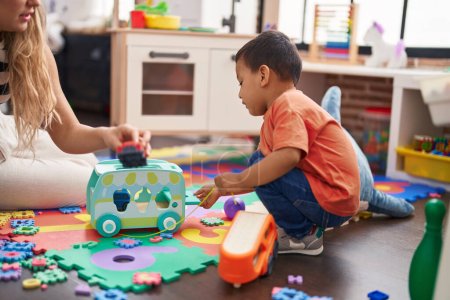 Téléchargez les photos : Teacher and toddler playing with cars toy sitting on floor at kindergarten - en image libre de droit