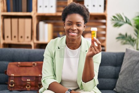 Foto de African american woman working on depression holding pills looking positive and happy standing and smiling with a confident smile showing teeth - Imagen libre de derechos