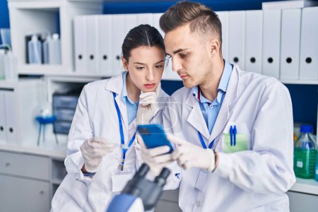Photo for Man and woman scientists using smartphone looking sample at laboratory - Royalty Free Image