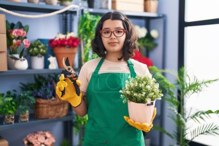 Téléchargez les photos : Young hispanic woman working at florist shop relaxed with serious expression on face. simple and natural looking at the camera. - en image libre de droit